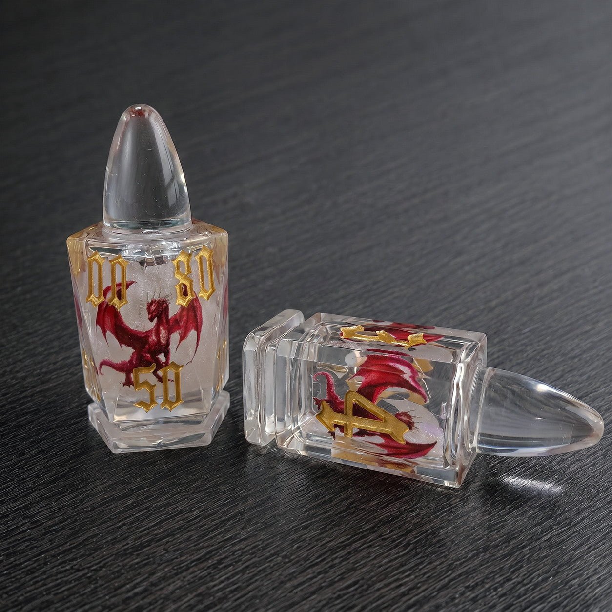 Dragonshot close-up of two clear bullet-shaped liquid core DND dice with red dragon motifs on a dark tabletop.