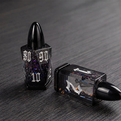 Midnight Assassin close-up of two black bullet-shaped liquid core DND dice with iridescent flakes on a dark tabletop.