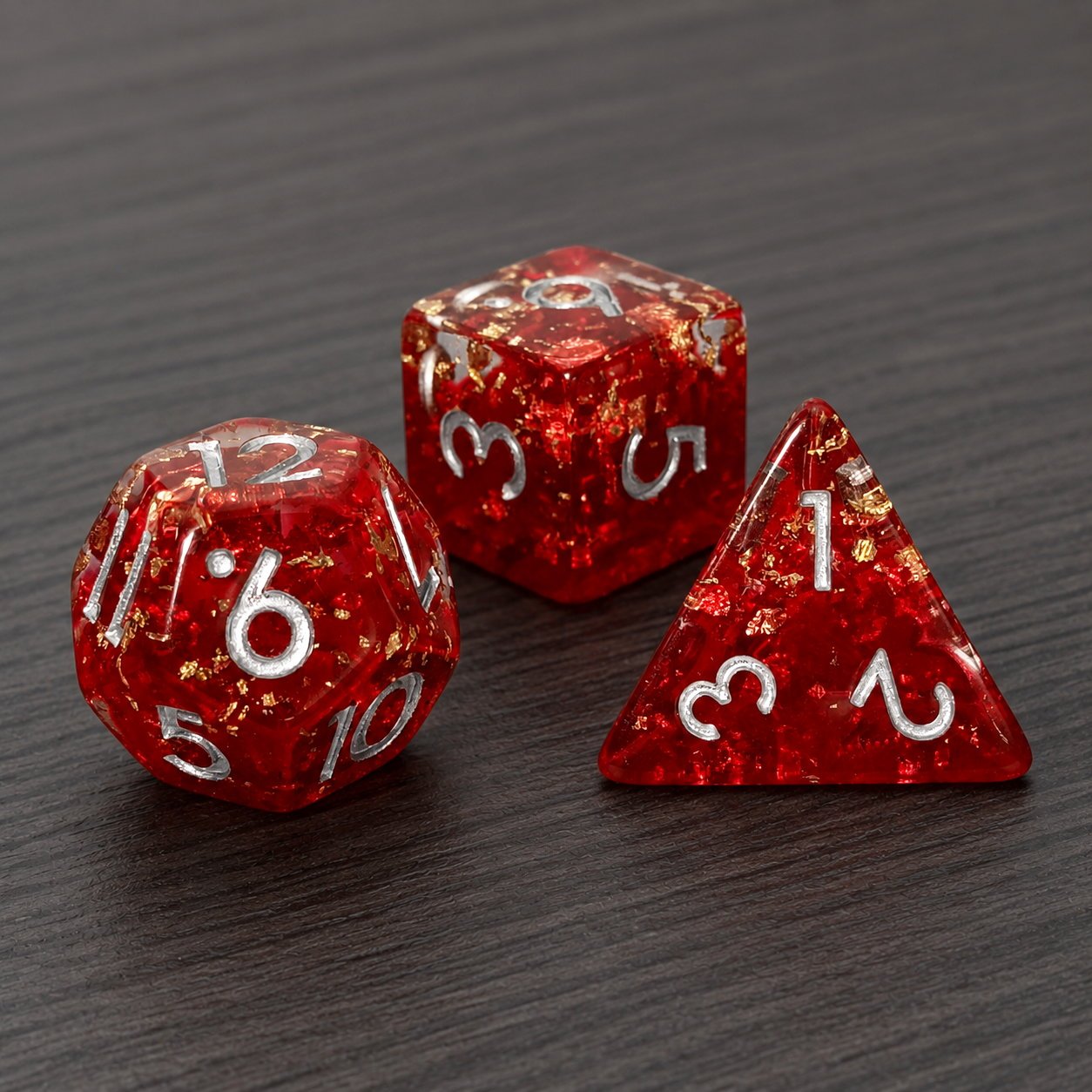 Phoenix Rebirth close-up of three red resin DND dice with gold foil flakes on a dark wood tabletop.