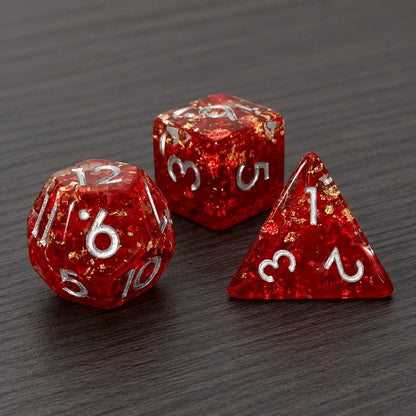 Phoenix Rebirth close-up of three red resin DND dice with gold foil flakes on a dark wood tabletop.