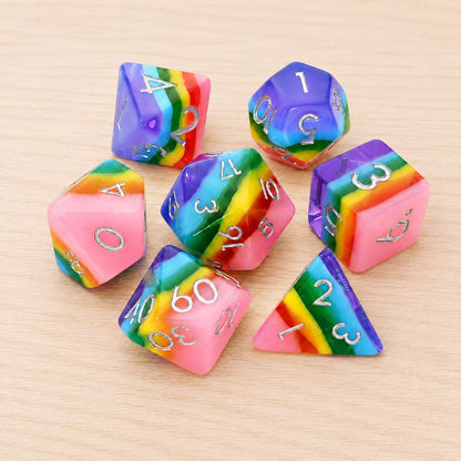 Rainbow Candy 7-piece rainbow layered resin DND dice set with silver numbers on a light wood tabletop.