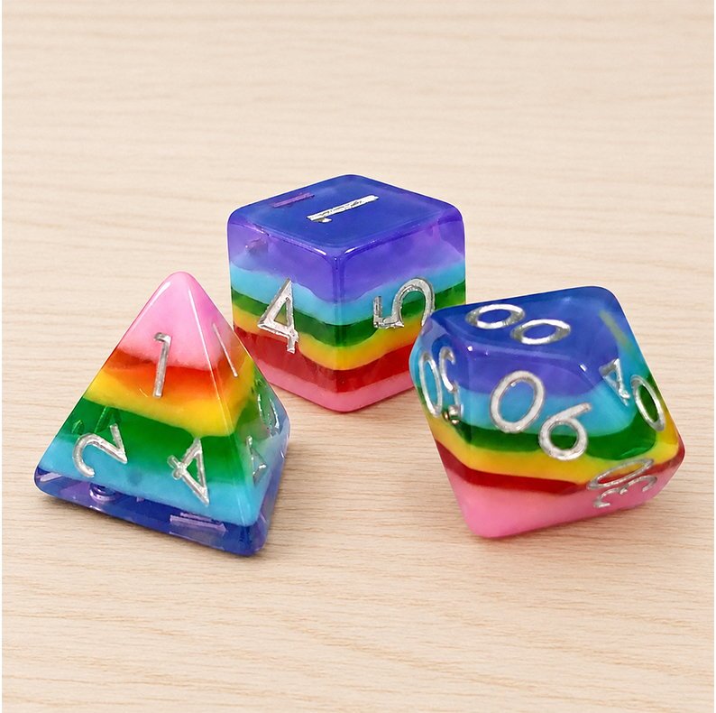 Rainbow Candy close-up of three layered resin DND dice with silver numbers on a light wood tabletop.