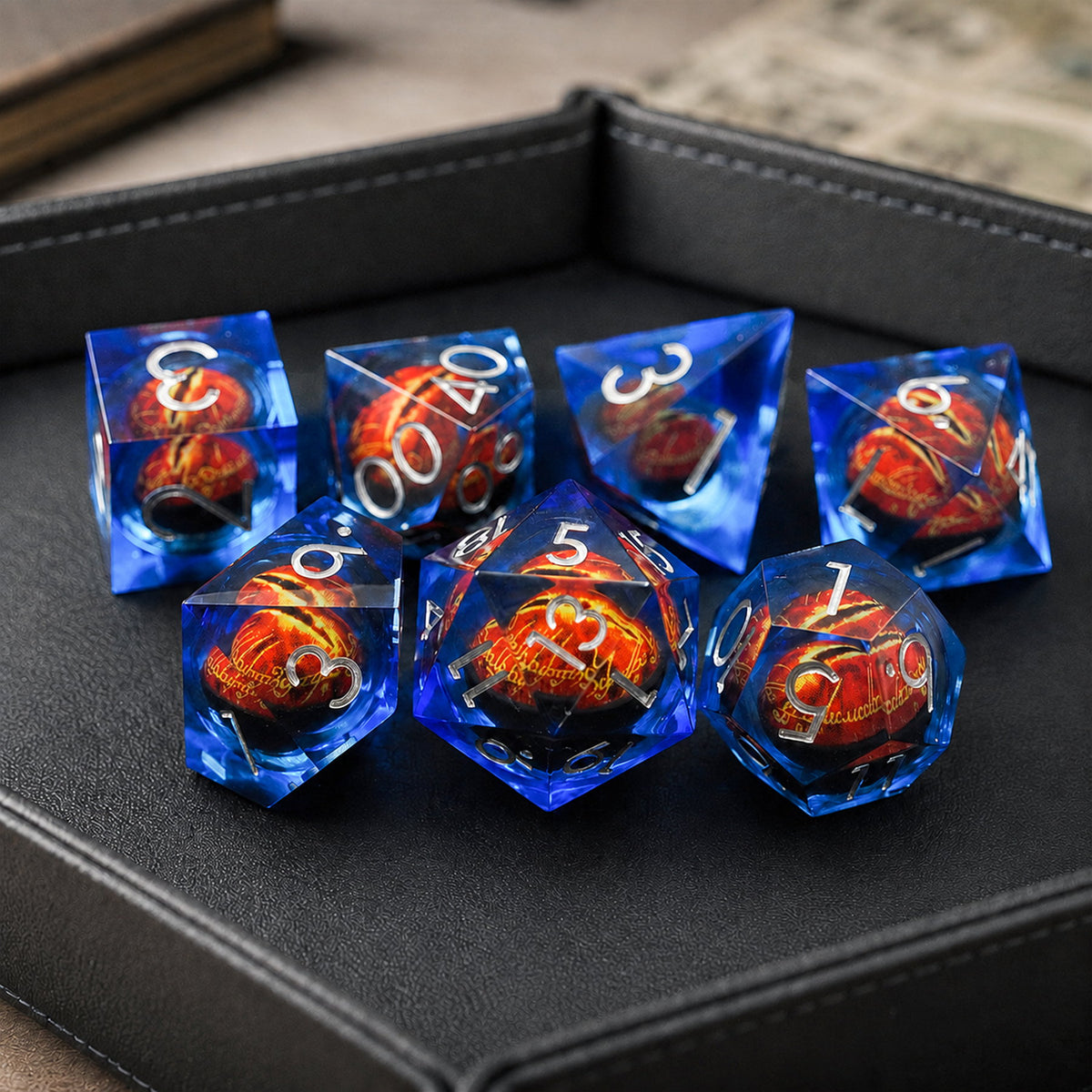 Sapphire Flame Dragon Eye 7-piece blue liquid core DND dice set with red dragon eyes and silver numbers in a black dice tray.