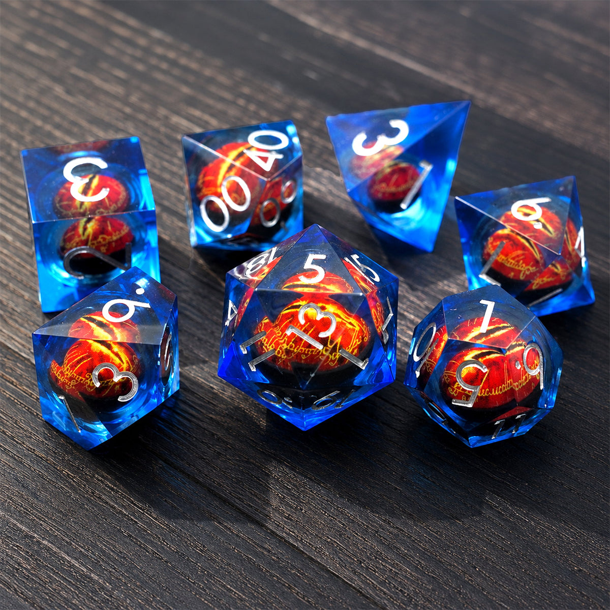 Sapphire Flame Dragon Eye 7-piece blue liquid core DND dice set with red dragon eyes and silver numbers on a dark wood tabletop.