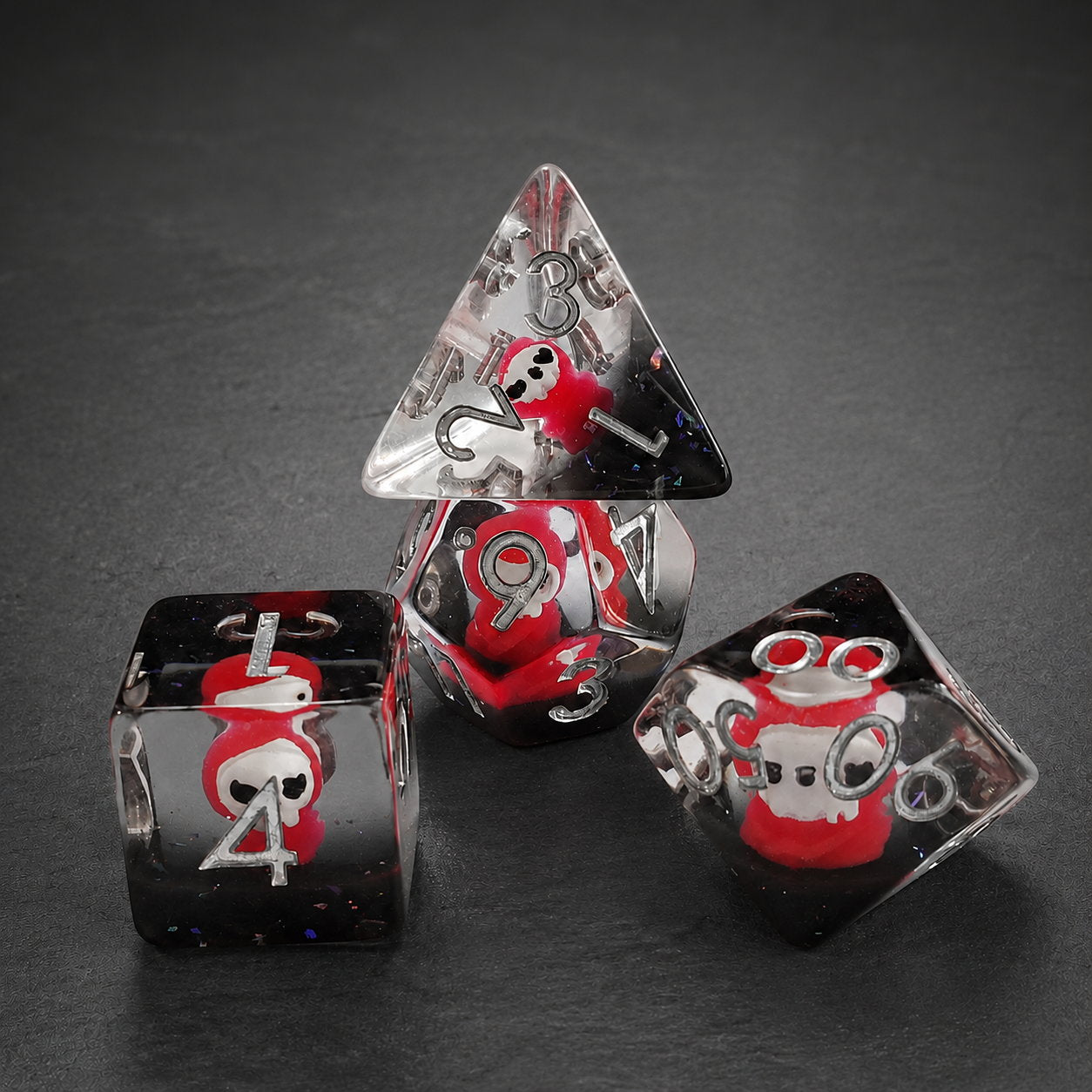 Scarlet Reaper close-up of four clear resin embedded DND dice with scarlet reaper figures on a dark background.